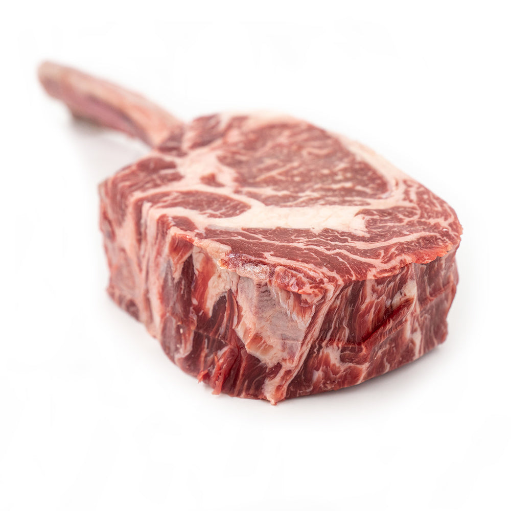 A thick, bone-in Tomahawk steak with rich marbling and a long rib bone, expertly cut and displayed on a clean, crisp white surface, showcasing its exceptional quality and tender texture.