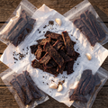 Pile of peppered Hassell Wagyu jerky with clear 4 oz bags on a ranch table